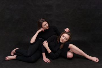 Fototapeta na wymiar Concept portrait of two stylish brunette sisters on a black background in various poses. Fashionable photo of two beautiful girls with dark hair