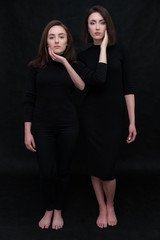 Concept portrait of two stylish brunette sisters on a black background in various poses. Fashionable photo of two beautiful girls with dark hair