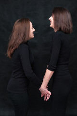 Concept portrait of two stylish brunette sisters on a black background in various poses. Fashionable photo of two beautiful girls with dark hair