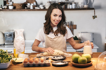 Cheerful young woman wearing apron preparing dough