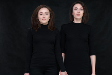 Concept portrait of two stylish brunette sisters on a black background in various poses. Fashionable photo of two beautiful girls with dark hair