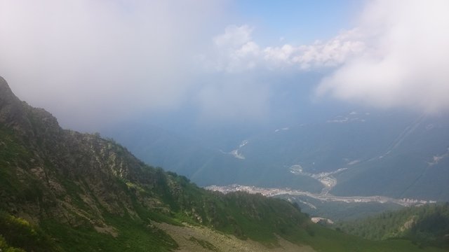 The tops of the high mountain slope of the black pyramid, with a cable car in front of which is the valley. Blue sky in the mountains on a summer day. Krasnaya Polyana, Sochi, Russia.