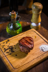 Grilled pork rib chop steak in a clay plate with oil, mustard, salt and rosemary is an old wooden table.