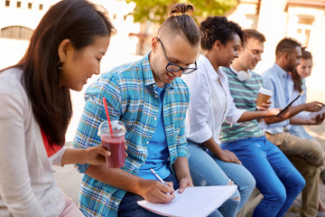 education and people concept - group of happy students with notebook and takeaway drinks learning...
