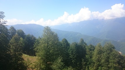 The tops of the high mountain slope of the black pyramid, with a cable car in front of which is the valley. Blue sky in the mountains on a summer day. Krasnaya Polyana, Sochi, Russia.