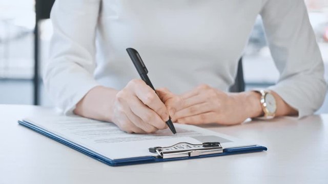 cropped view of woman filling and signing document with resume lettering in office 