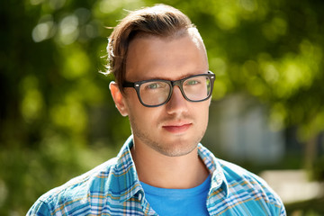 people and style concept - portrait of young man in glasses outdoors in summer