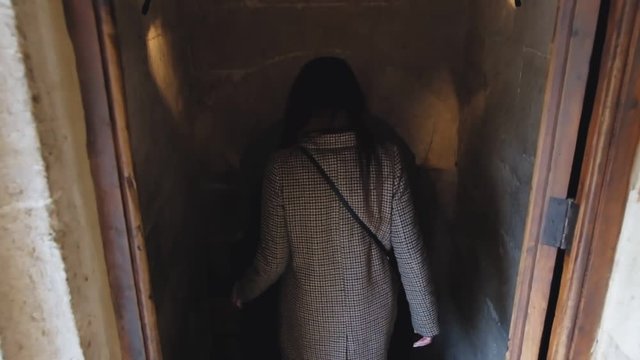 Slow motion of the woman's back going down to the basement of the old castle