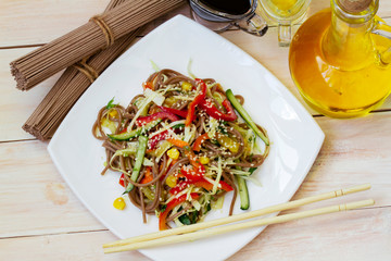 Japanese soba salad with vegetables and sesame close-up on a plate on the table. horizontal top view from above. vegetarian Asian food. noodles salad. buckwheat noodle with vegetables.