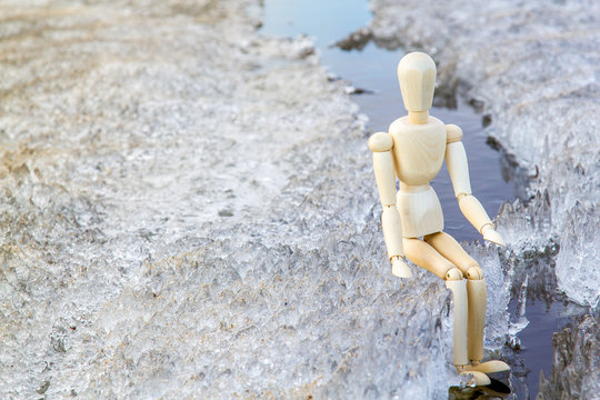 Gestalta figure sits on the edge of melting ice on the lake