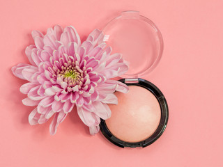 Powder or highlighter in a round package on a pink background with a flower.