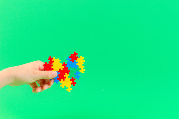 Child hand holding colorful heart on green background. World autism awareness day concept