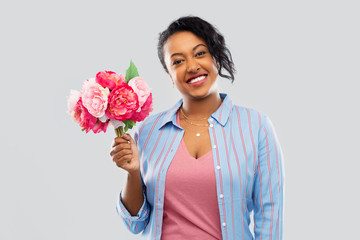 people and international women's day concept - happy african american young woman with bunch of peony flowers over grey background