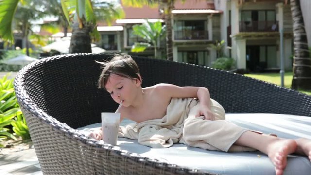 Cute boy, drinking choco milkshake on the pool deck while on holiday on tropical island of Mauritius
