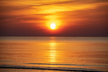 Obraz premium orabge colored sunset over calm sea beach water fields