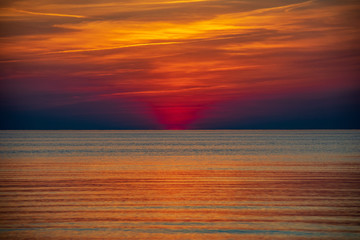 orabge colored sunset over calm sea beach water fields