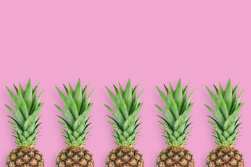 Fototapeta premium Row of fresh pineapples with green leaves lying on pink table on kitchen. Top view. Cooking concept