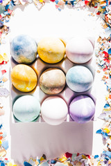 Colored eggs container with different colored egg, circled by pieces of broken eggs,  easter concept, hard natural direct light