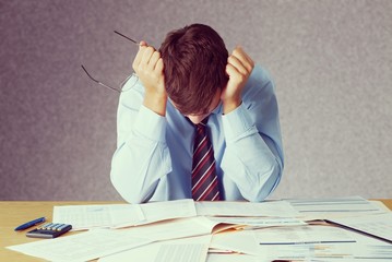 Tired young business man with a lot of  papers on the table