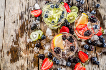 Summer fruits and berry cold cocktail, Lemonade, infused water with blueberries, strawberries, blackberries, kiwi. lemon. Rustic wooden background copy space