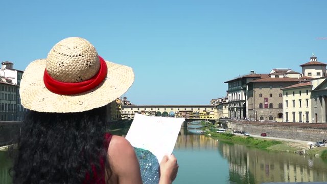 Smiling tourist with city map visiting Ponte Vecchio in Florence, Italy. Happy woman travels to best place of Tuscany, cheerful girl visiting buildings. Must see sightseeing of Firenze, Italian tour