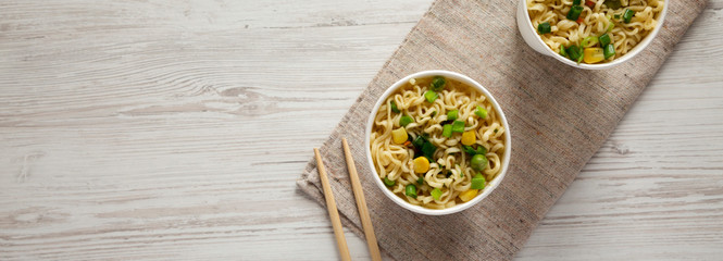 Top view, instant ramen noodles in paper cups over white wooden background. Flat lay, overhead, from above. Copy space.