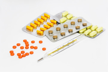 multi-colored yellow orange brown pills and a temperature thermometer on a white background