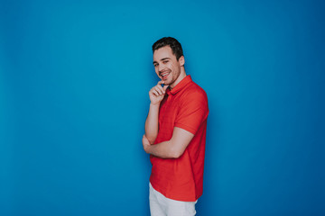 Happy Caucasian man touching chin and looking at camera on blue background