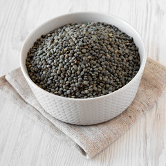 Dry green french lentils in gray bowl over white wooden background, low angle view. Close-up.