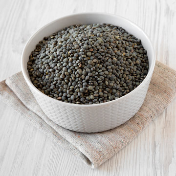 Dry green french lentils in gray bowl over white wooden background, low angle view. Close-up. © Liudmyla