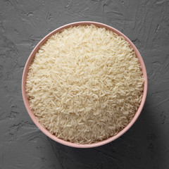 Dry white rice basmati in a pink bowl over concrete surface, top view. Flat lay, overhead, from above.