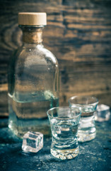 Two shots and a bottle of vodka on wooden background