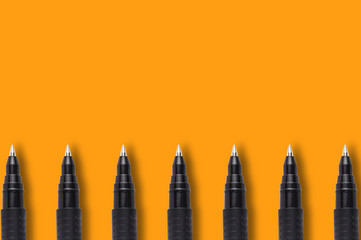 Row of black and green plastic pens on orange background with copy space for your text. Top view