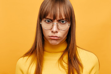 Fototapeta premium Woman portrait. Emotion. Beautiful young woman in eyeglasses is pouting her lips at camera, on a yellow background