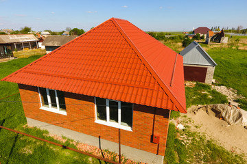House with an orange roof made of metal, top view. Metallic profile painted corrugated on the roof.
