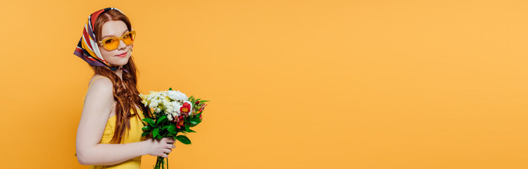 Naklejka premium panoramic shot of beautiful stylish girl in headscarf and sunglasses holding flowers isolated on yellow with copy space