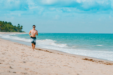 Man running on the beach during summer. Doing cardio exercise on the sand. Photo at Praia de Tabatinga 2, Conde PB Brazil. 