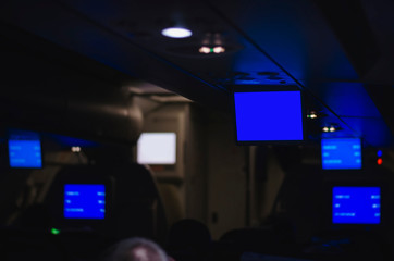 Fototapeta na wymiar Inside an airplane during a flight with the informative tv screens down. Plane with low light, tvs with a informative blue screen.