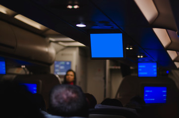 Inside an airplane during a flight with the informative tv screens down. Plane with low light, tvs with a informative blue screen.