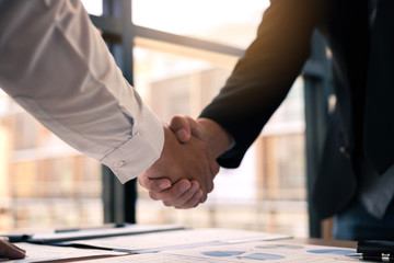 Entrepreneurs collaboration deal shaking hands in a modern office and financial paper graph on desk.