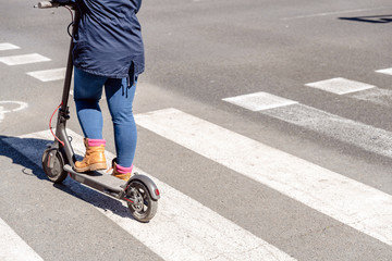 Detail of an electric scooter driven by a woman while waiting her turn to cross a road.