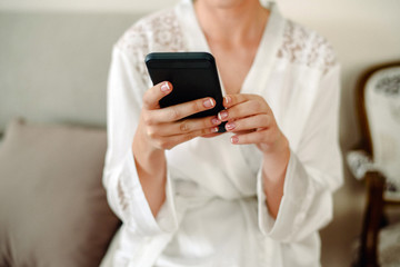 Woman consulting her mobile phone while waiting in white pajamas.