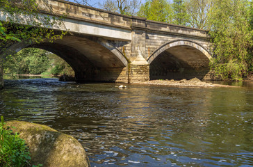 A stone bridge arches over a tranquil flowing river on an idyllic summers day