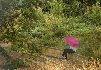 A young woman sits under a pink umbrella in a nature reserve checking her phone