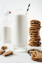 selective focus of glass with fresh milk and straw near chocolate cookies and bottle on marble table