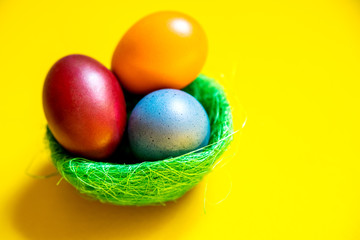 Easter colorful eggs in a green basket on a yellow background.