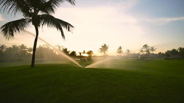 Golf course sprinkler on fairway during golden sunset
