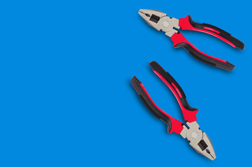 Two new metal pliers with rubber handles black and red color on blue table with copy space for your text. Top view. Repair or building concept
