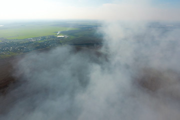 Fototapeta premium The smoke over the village. Clubs of smoke over the village houses and fields. Aerophotographing areas