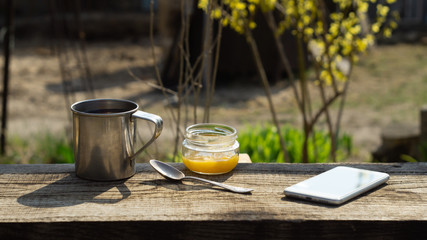 Metal mug, a jar of honey and a telephone on a wooden table